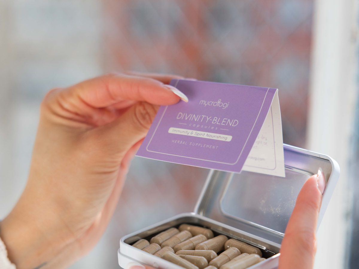 Hands opening a tin of Divinity Blend capsules.