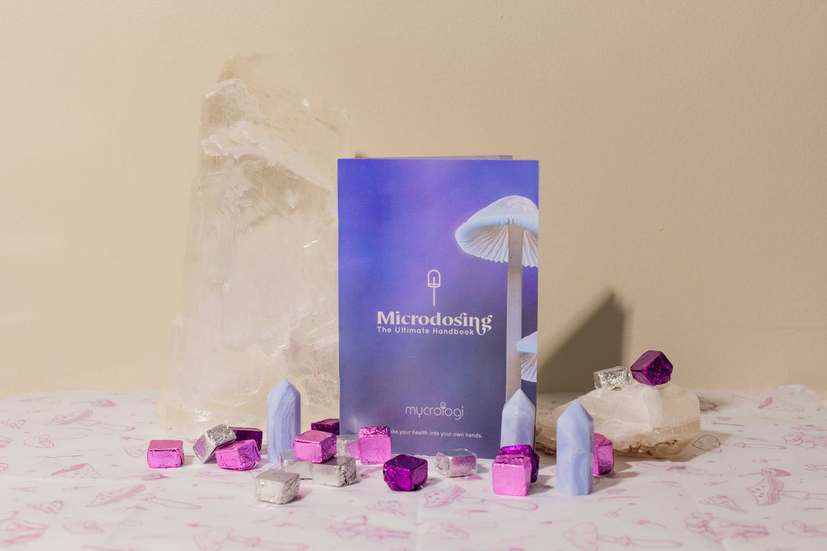 The Mycrologi Microdosing Handbook standing on a warm cream surface with quartz.