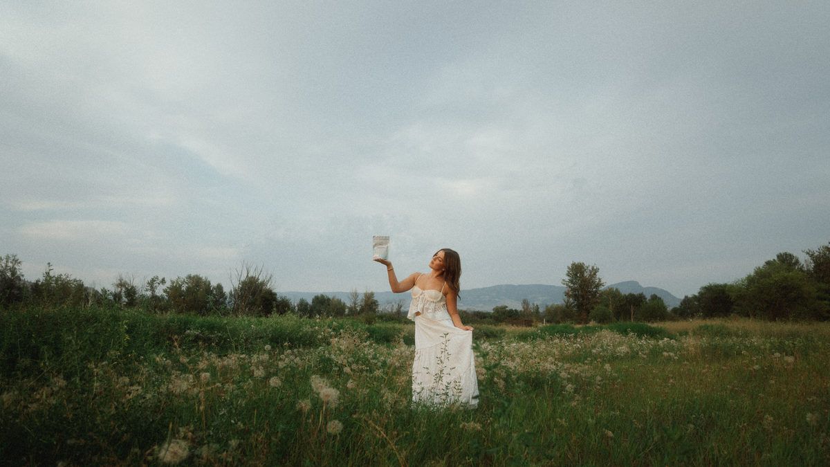 A woman standing in a wide summer meadow under an open sky.