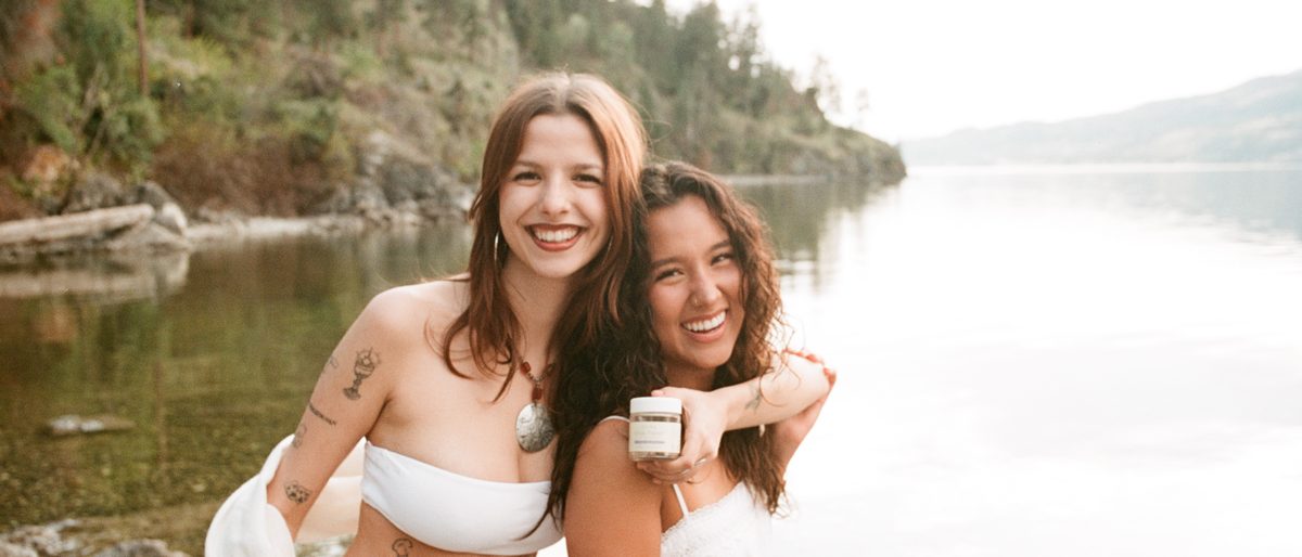 Two people laughing together at the edge of a calm lake.