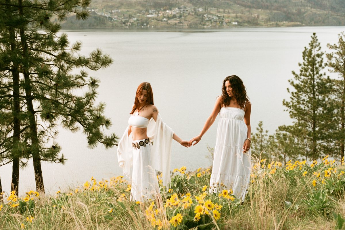Two people walking hand in hand through a wildflower meadow beside a lake.