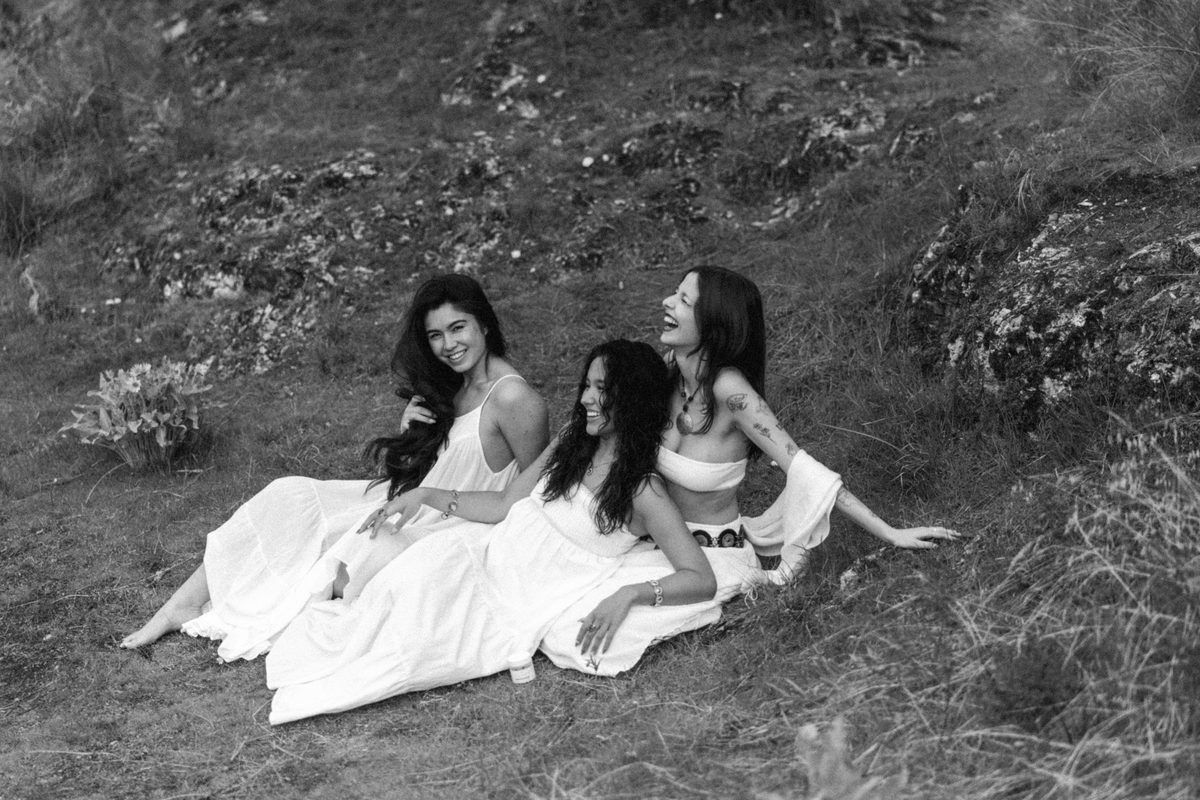 Three people sitting together on a grassy hillside, shot on black and white film.