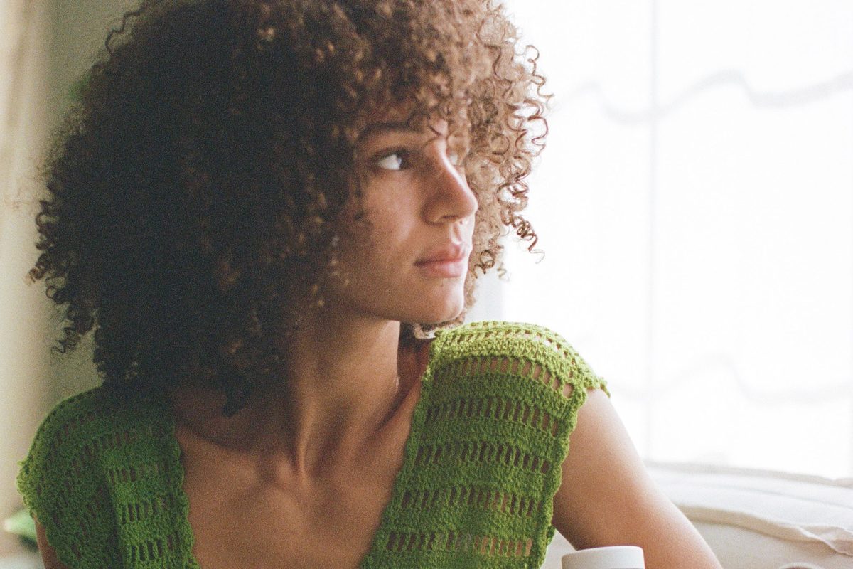 A person in a green knit top sitting beside a bright window.