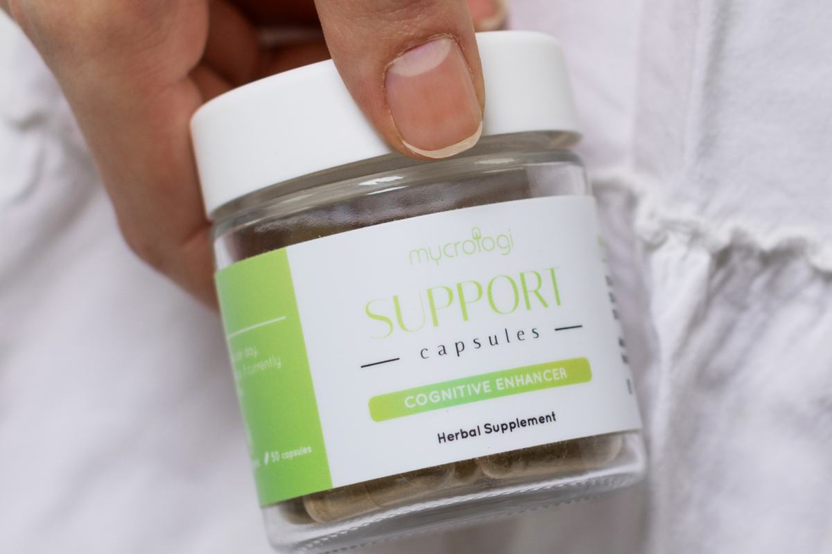 A hand holding a jar of Mycrologi Support Capsules
