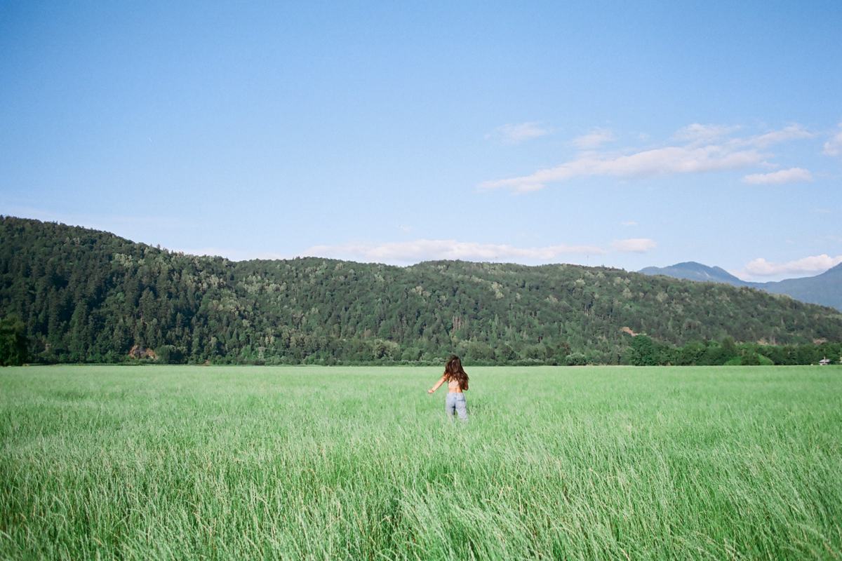 A lone figure walking through a wide green field below the mountains