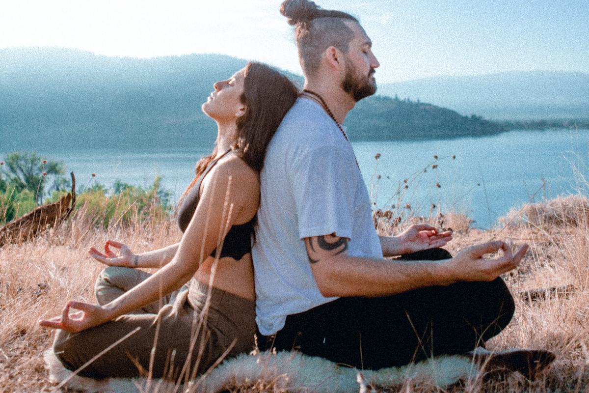 Two people sitting back to back on a hillside above a lake